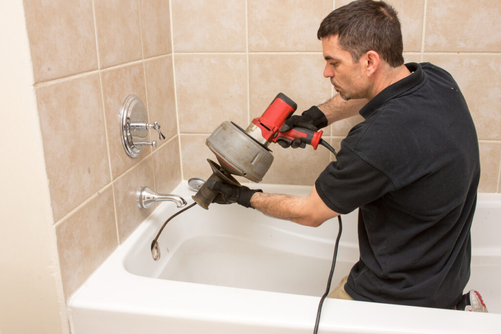 Plumber unclogging tub drain with auger